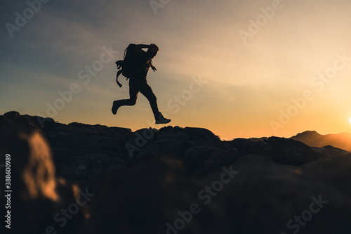Hiker on top of a mountain Running on the ridge of the mountain with beautiful golden hour sunset with intense color and blue sky fused with yellow, carries a large backpack