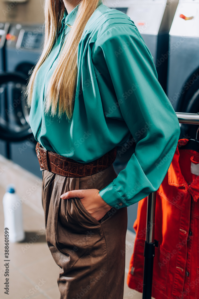 cropped view of stylish woman standing with hand in pocket in laundromat