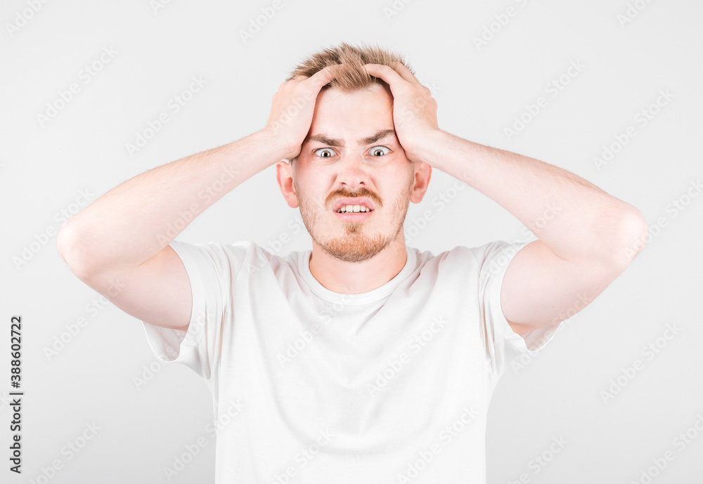 Embarrassed fashionable young man being afraid of difficulties, stands against white background Embarrassed fashionable young man being afraid of difficulties, stands against white background