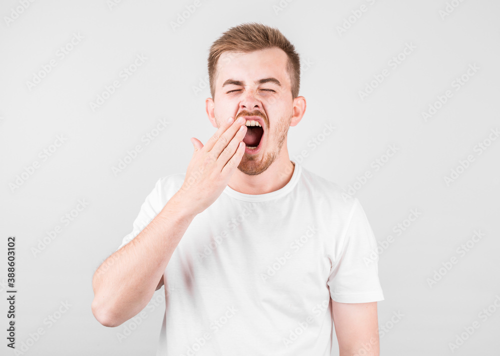 Tired young guy yawning, feeling sleepy, covering mouth with hand, feeling lack of energy, rest or relax, head shot Tired young guy yawning, feeling sleepy, covering mouth with hand, feeling lack of energy, rest or relax, head shot