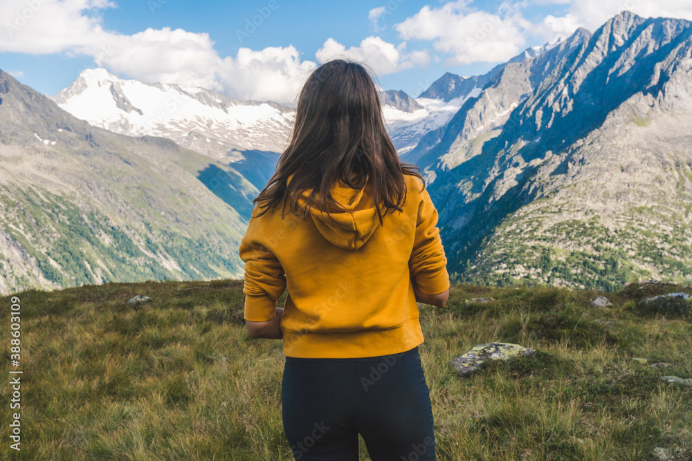 Young backpacker boy with the back at the camera watching a beautiful view over a lake in the Alps, scenic mountains in the background