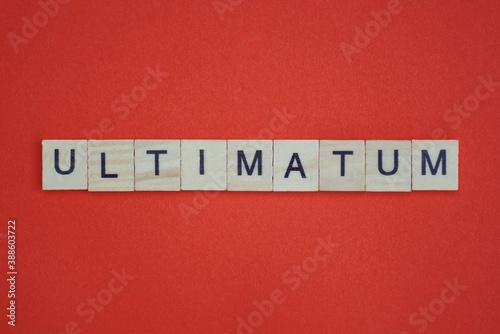 text the word ultimatum from gray wooden small letters with black font on an red table photo