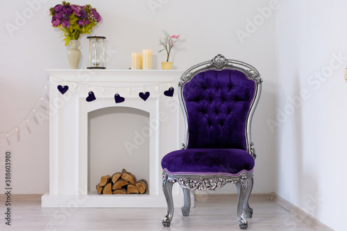 Purple chair against the background of the fireplace, a candle on the fireplace and a bouquet of flowers