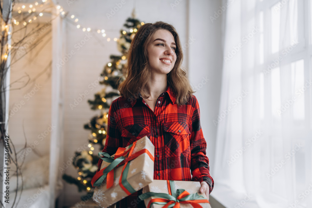 Pretty woman in shirt and socks walking at home with christmas gift box, new year tree behind. Pretty woman in shirt and socks walking at home with christmas gift box, new year tree behind.