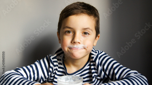 Boy in striped t-shirt with a mustache from kefir or milk in the grey background and glass in his hand