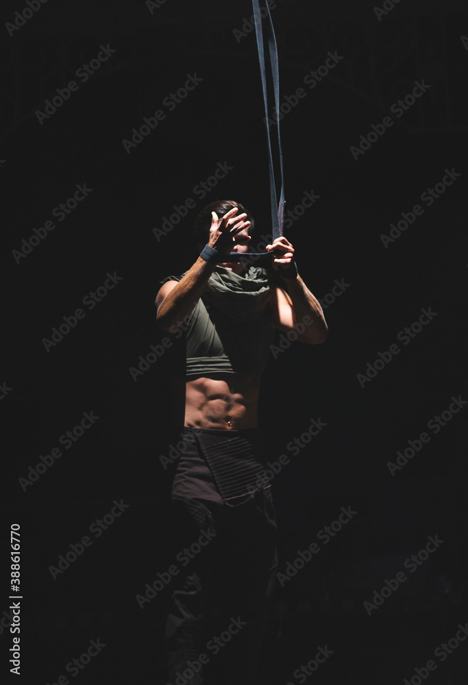 Muscular acrobat in the dark prepares ropes for an exercise. Muscular acrobat in the dark prepares ropes for an exercise.