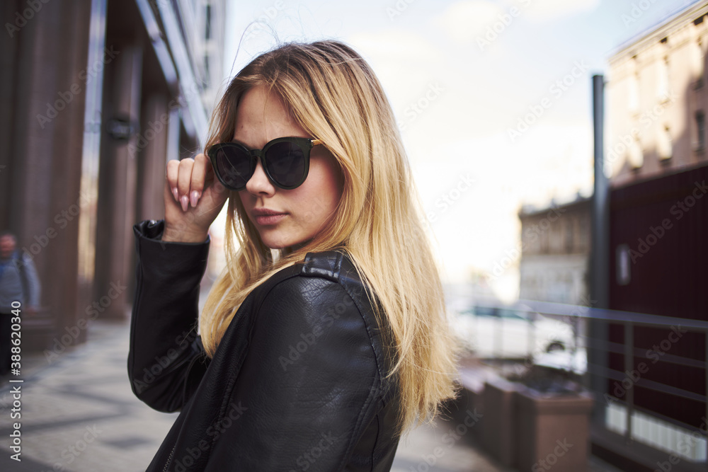 Fashionable woman in a leather jacket and sunglasses near the building Fashionable woman in a leather jacket and sunglasses near the building