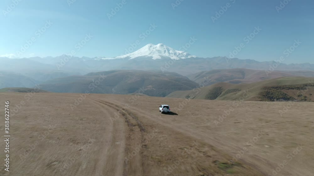 Tourist suv car driving on highland field on mountain Elbrus peak background. Predator eagles birds flying over mountain valley for hunting. Wild animal nature in picturesque Kabardino-Balkaria Tourist suv car driving on highland field on mountain Elbrus peak background. Predator eagles birds flying over mountain valley for hunting. Wild animal nature in picturesque Kabardino-Balkaria
