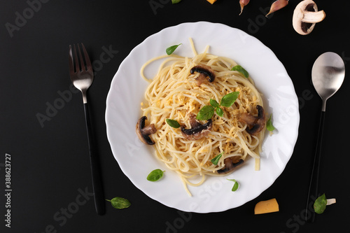 Spaghetti with mushrooms and basil on white plate on black background, Top view, Space for text photo