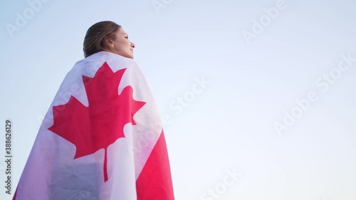 A person with a flag on shoulders looks proudly into the distance. Clear skies in the background. Canadian flag