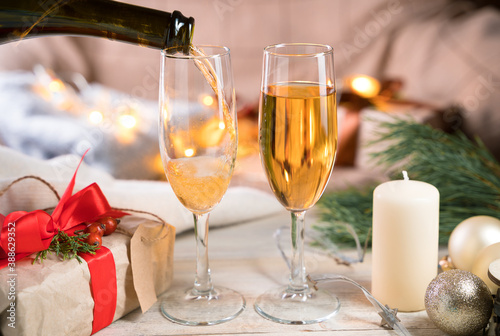Two glasses and a bottle of champagne, the process of pouring champagne into glasses in the room in a cozy atmosphere. The concept of Christmas holidays.