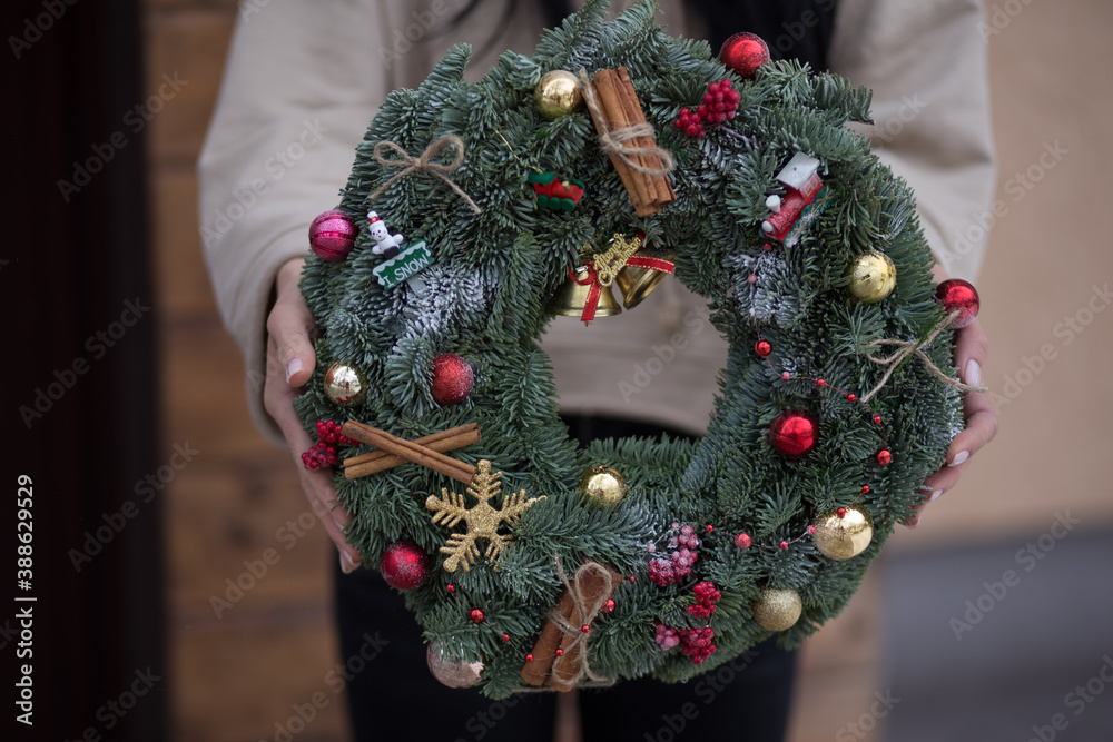 The girl holds a beautiful Christmas wreath decorated with toys and ornaments that she made herself