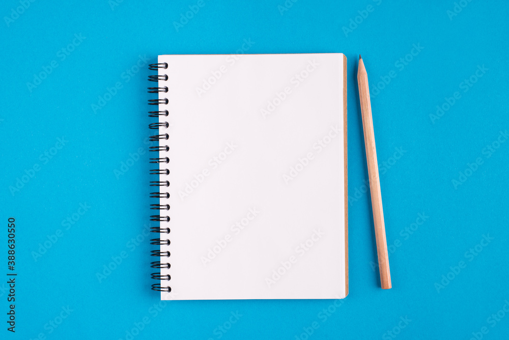 Above top overhead close up view photo of opened memory pad with blank page and wooden pencil isolated over bright color blue background with copy space Above top overhead close up view photo of opened memory pad with blank page and wooden pencil isolated over bright color blue background with copy space