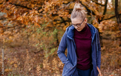 Girl with glasses in the autumn forest. Woman with a a basket walks in the woods. Autumn walk.