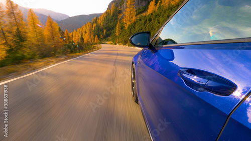 CLOSE UP: Brand new sportscar speeds down mountain road in the Alps at sunset.