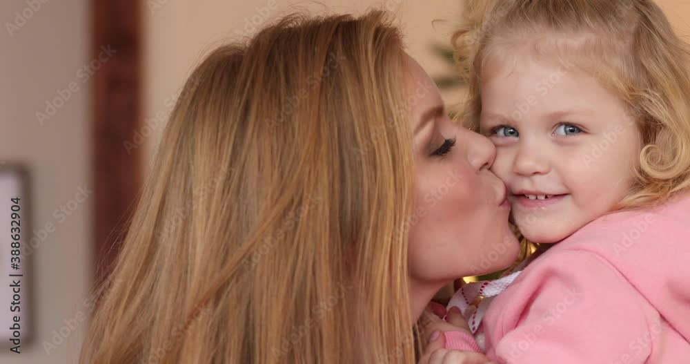 Happy mother holding and kissing her daughter with a Christmas tree in the background Happy mother holding and kissing her daughter with a Christmas tree in the background