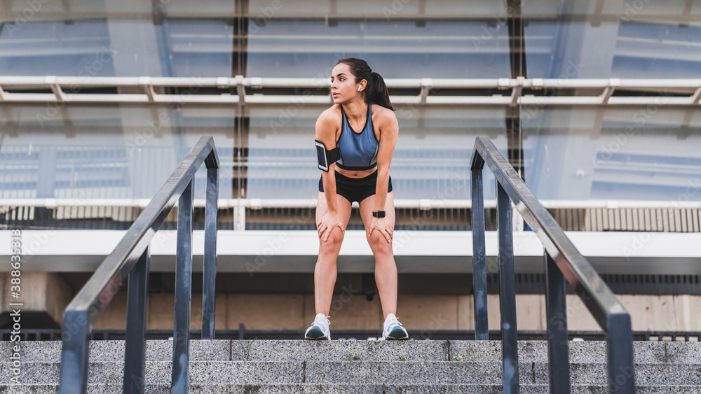 Full length horizontal portrait of a sporty girl in fitness outfit standing on the stairs in urban area