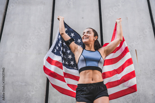 Low angle view photo of 20s happy female athlete holding American flag against grey wall photo