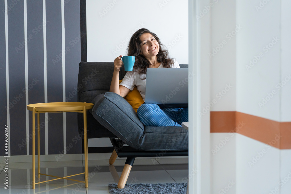 Beautiful girl sitting with a laptop on a sofa in a stylish room. Work from home. Work atmosphere in a good mood Beautiful girl sitting with a laptop on a sofa in a stylish room. Work from home. Work atmosphere in a good mood