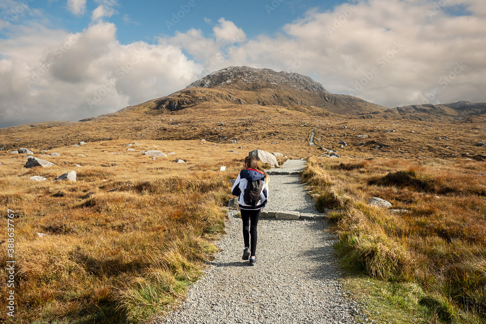 Teenager girl on a path to a mountain peak, Diamond hill in Connemara National park, county Galway, Ireland, Bright sunny day, blue cloudy sky.