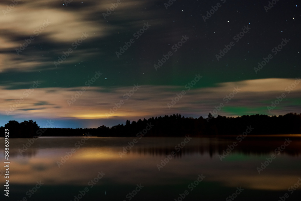 Northern Lights or aurora borealis over the lake in cloudy sky. 