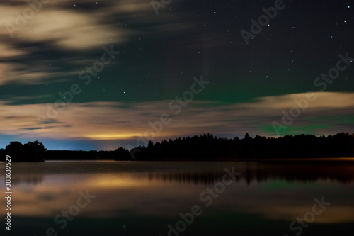 Northern Lights or aurora borealis over the lake in cloudy sky. 