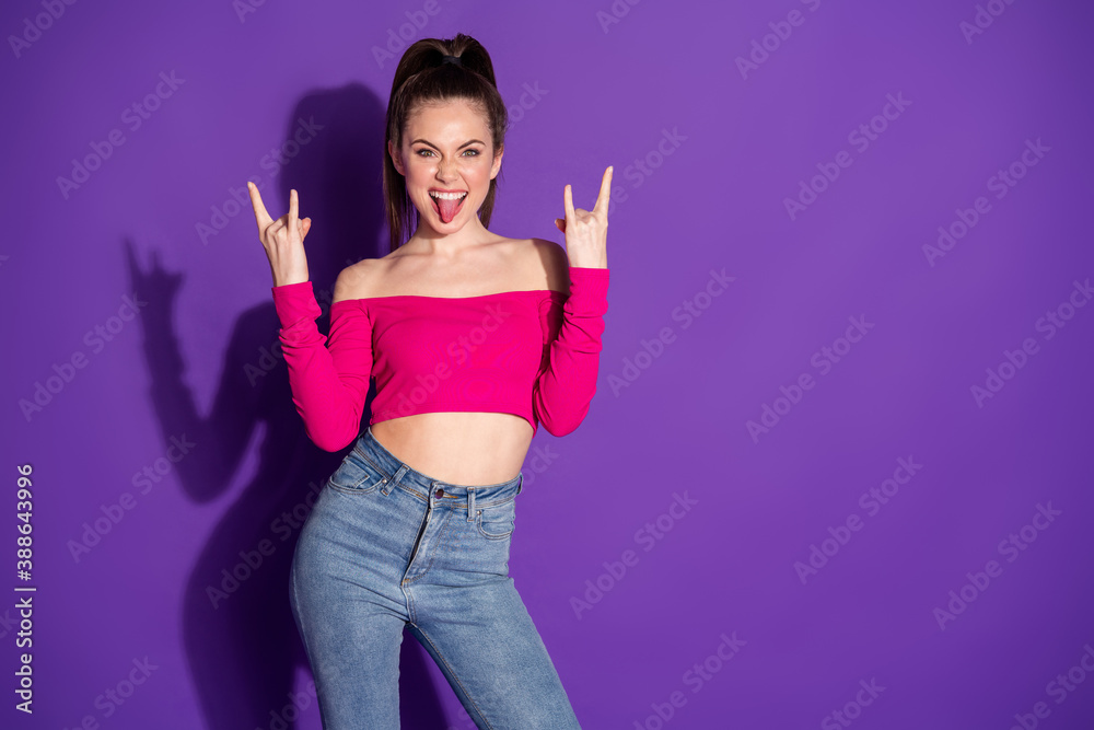 Photo of funky lady raise two arms show horns stick out tongue look camera wear jeans pink cropped top isolated purple color background Photo of funky lady raise two arms show horns stick out tongue look camera wear jeans pink cropped top isolated purple color background