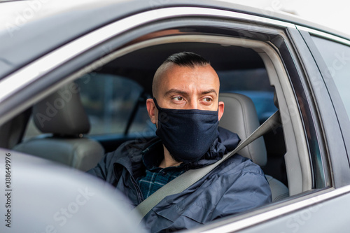 second wave coronavirus man driving a car puts on a black mask during an epidemic, driver in a mask, protection from the virus. Driver in black car. , disease, infection, quarantine, covid-19 © drotik