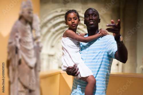 Positive Afro father and daughter looking at exhibits of medieval sculpture on exposition of museum