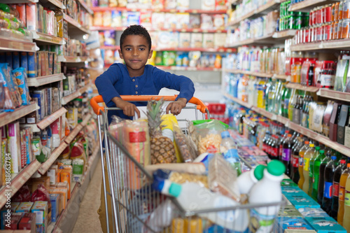 Portrait of cute African boy with shopping cart full of food products in store