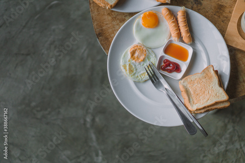Breakfast with fried eggs Sausage and bread in a white plate are placed on a wooden table.