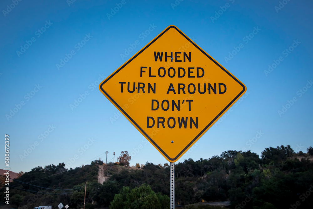 A yellow and black diamond shaped traffic sign warning about drowning in a flood.