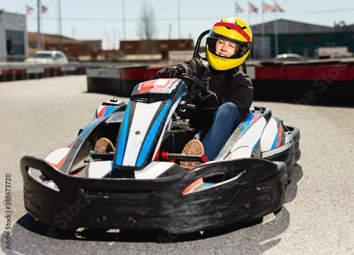 Portrait of fine female in helmet driving racing car at outdoors cart circuit