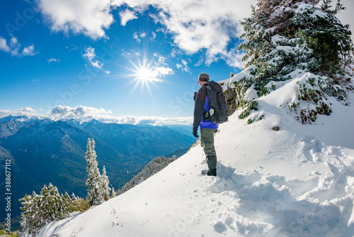 Adventurous male hiker standing on a mountain ridge in the snow looking out at the landscape.