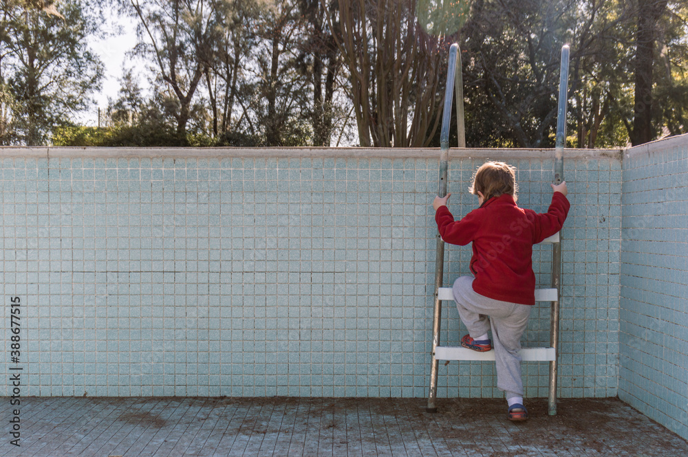 Unrecognizable child climbing an empty pool ladder