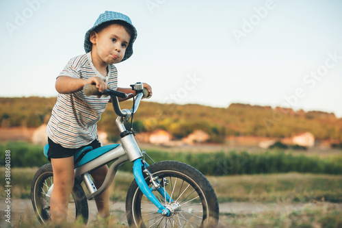 Concentrated caucasian boy with blue hat and bike looking somewhere in a field during a summer walk photo