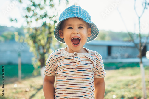 Happy caucasian boy in a blue hat is laughing at camera while playing in the backyard of the house photo