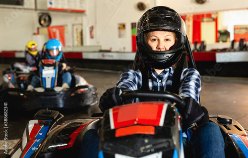 Cheerful positive smiling girl and her friends competing on racing cars at kart circuit