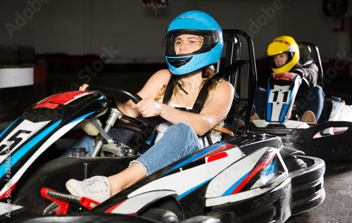 sportive adulr woman in helmet driving car for karting with other people in sport club indoor © JackF