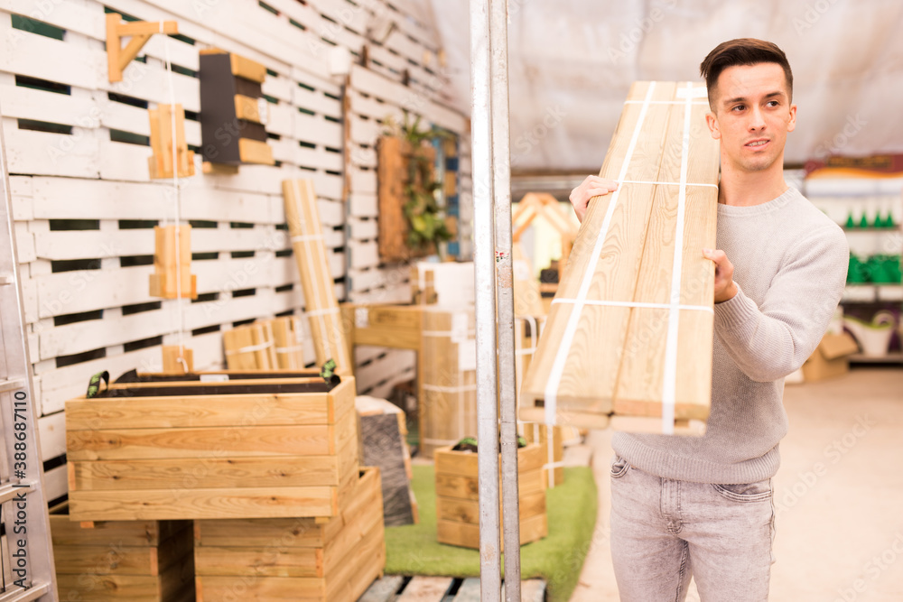 Portrait of guy buying wooden boards for bench in garden market..