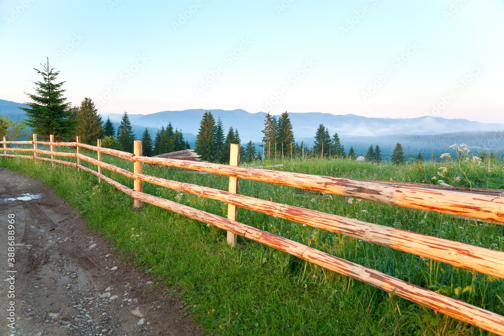 Summer mountain landscape, road and wooden fence, foggy mountains on the horizon.