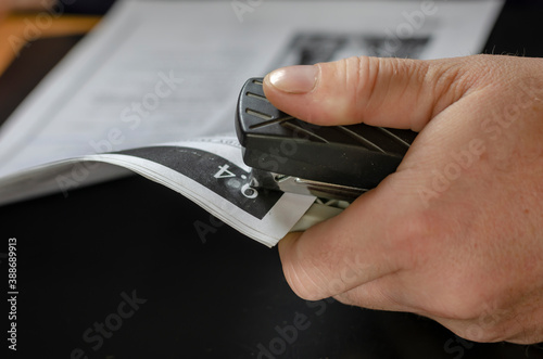 Fotografie Men's hands staple up a pile of paper with printed text.