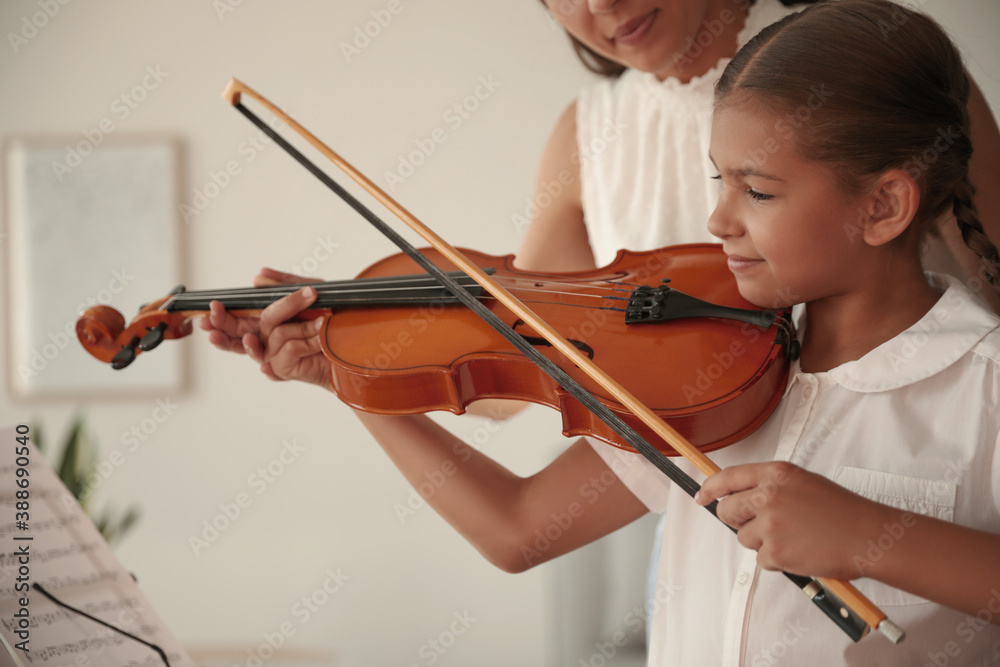 Young woman teaching little girl to play violin indoors Young woman teaching little girl to play violin indoors