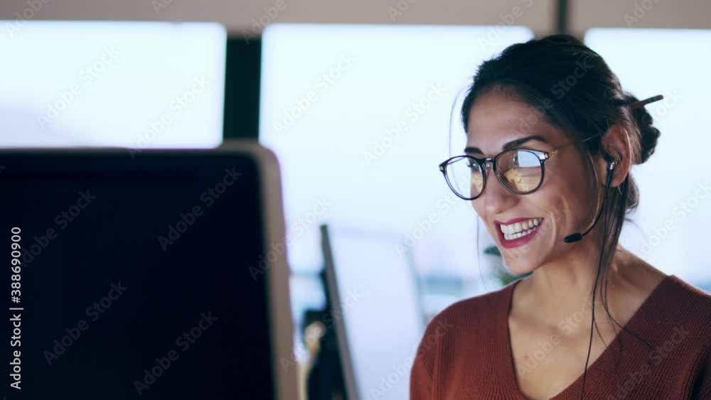 Shot of beautiful young business woman working with computer while talking with earphone sitting in the office.
