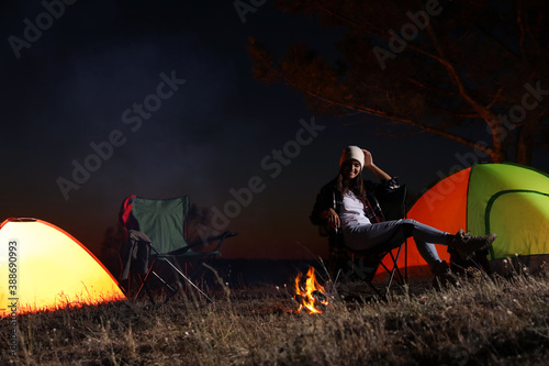 Young woman sitting near bonfire at night. Camping season