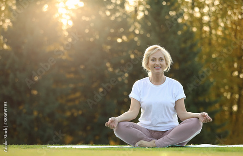 Mature woman practicing yoga on green grass in park