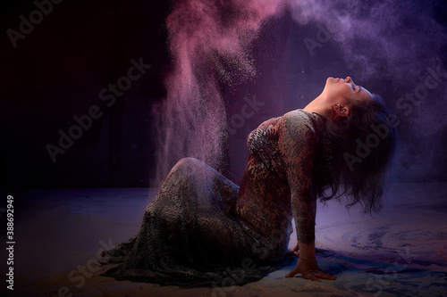 Girl in black dress posing in dark studo during photoshoot with flour or dust and light. Dangerous witch during struggle between good and evil photo