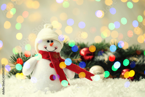 Cute snowman and fir tree branches with Christmas balls on snow, bokeh effect. Space for text © New Africa