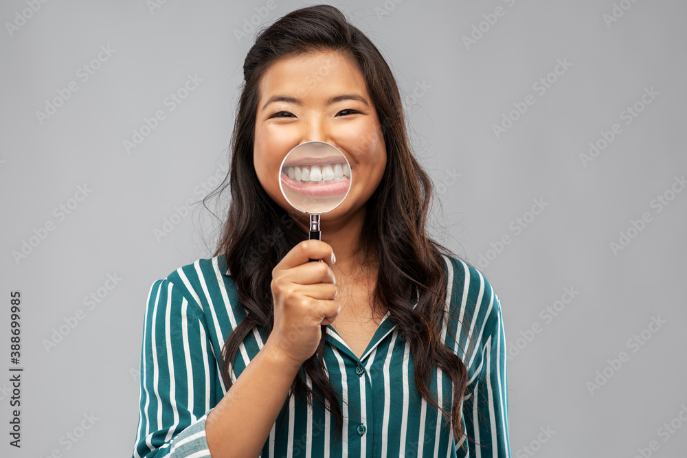 fun, dental care and people concept - happy asian woman showing her teeth through magnifying glass over grey background fun, dental care and people concept - happy asian woman showing her teeth through magnifying glass over grey background