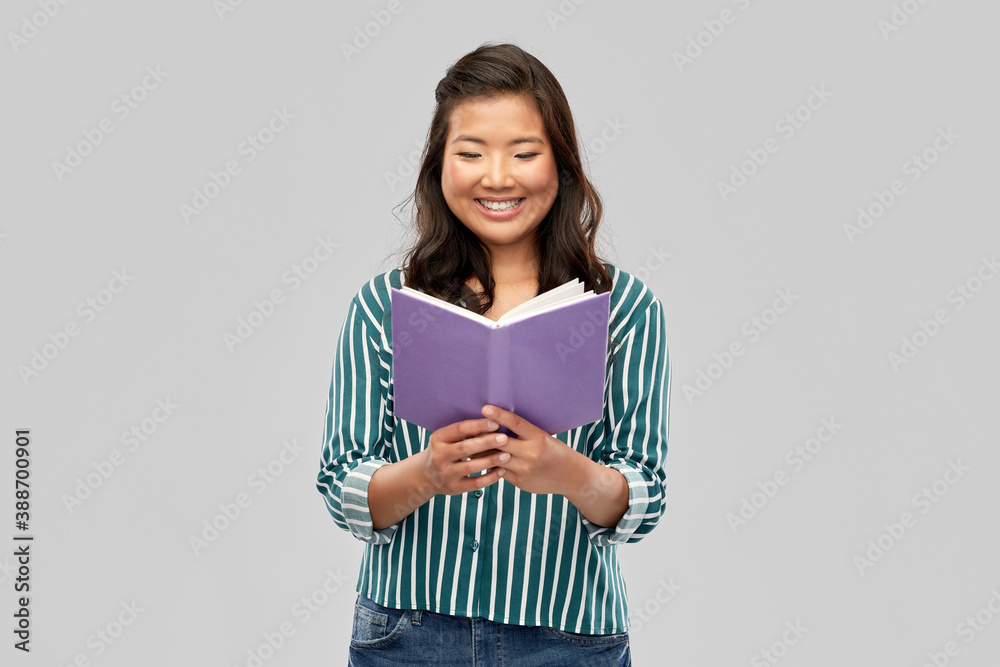 people, ethnicity and portrait concept - happy asian young woman reading book over grey background people, ethnicity and portrait concept - happy asian young woman reading book over grey background